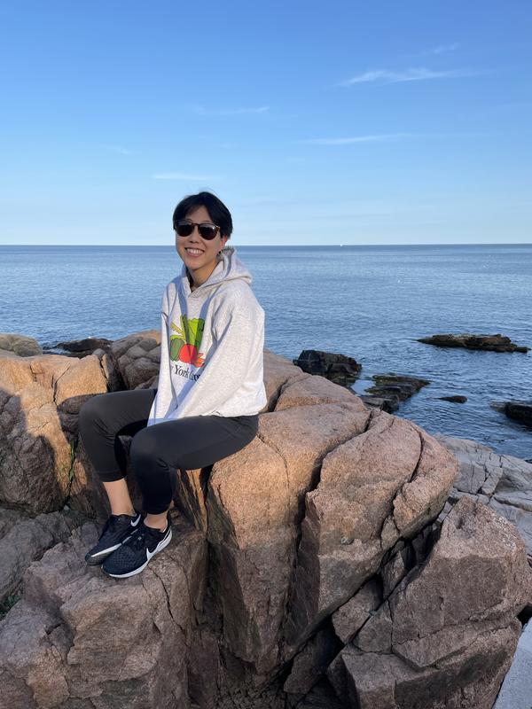 Jean Kim sitting on a rock in front of the ocean.