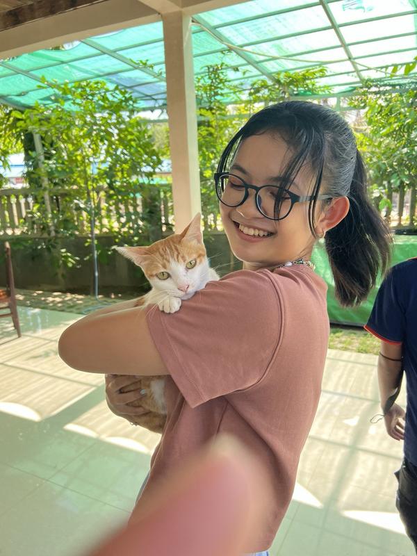 Rika Chan is outside wearing a red shirt and holding a cat.