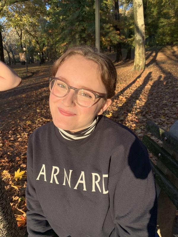 Margaret Barnsley wearing glasses with her hair tied back wearing a blue barnard sweater outside with leaves on the ground.